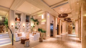 A spacious lobby with a modern design, featuring a staircase, seating area with white sofas, and a reception desk. - Incredible Ocean Views! 2 BR/2.5 Bath, On Top of 1 Hotel! 15th Flr, 4 Pools! (Miami Beach)