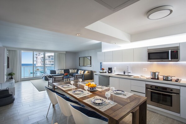 A modern kitchen with Bosch appliances, a dining area with a wooden table set for four, and a balcony with a view of the sea. - Incredible Ocean Views! 2 BR/2.5 Bath, On Top of 1 Hotel! 15th Flr, 4 Pools! (Miami Beach)