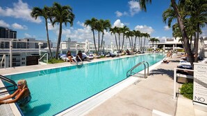 A pool area with lounge chairs and palm trees, surrounded by modern buildings. - Incredible Ocean Views! 2 BR/2.5 Bath, On Top of 1 Hotel! 15th Flr, 4 Pools! (Miami Beach)