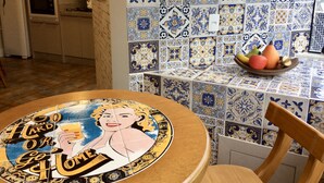 Una cocina con baldosas azules y blancas de diseño, una mesa de madera con mantel de estilo vintage y un frutero en la encimera.
