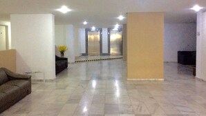 Un vestíbulo amplio con piso de mármol, un sofá, una mesita con un florero y dos ascensores.