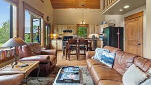 A spacious living room with leather sofas, a coffee table with magazines, and a dining area with wooden chairs and a table.