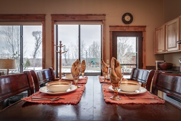 A dining table set for four with a view of a snowy landscape through large windows.