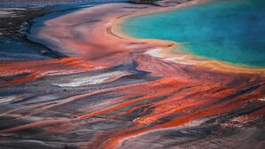 An aerial view of a geothermal area with distinct mineral deposits and a turquoise water body.