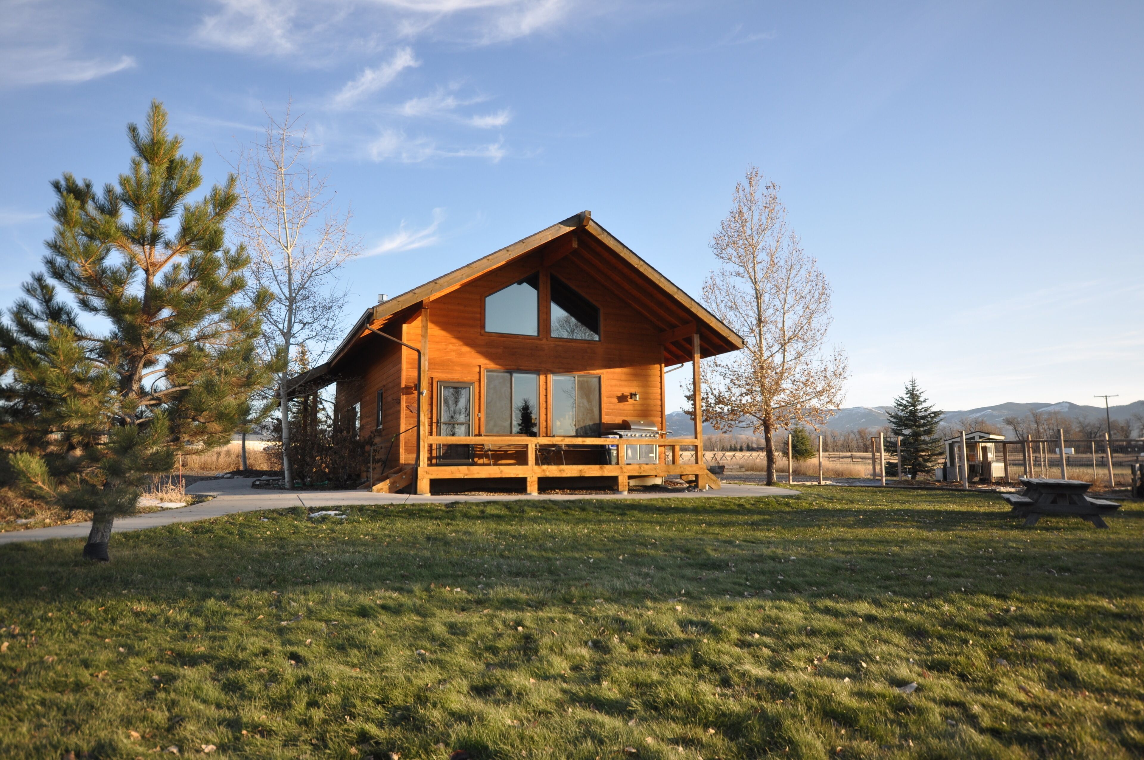 Eine Holzhütte mit großer Veranda, umgeben von einer Wiese und Bäumen.