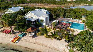 An aerial view of a beachfront property with a swimming pool, beach umbrellas, and kayaks.