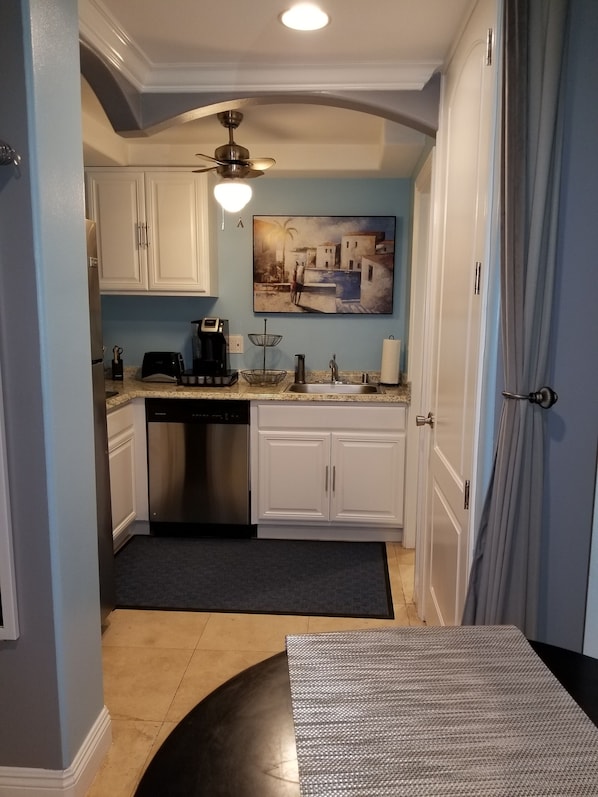 A modern kitchen with white cabinets, a black dishwasher, a coffee maker, and a painting on the wall.