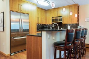 A kitchen with wooden cabinets, stainless steel appliances, and a bar area with stools. - 100 ft. to Gondola!! Balcony, Fireplace, Views, Parking!! Heart of Lionshead!! (Vail)