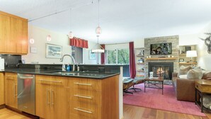 Eine moderne Küche mit Holzausstattung und einer Kochinsel, ein Wohnbereich mit Kamin und ein Essbereich mit rotem Teppich.