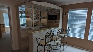 Una zona de bar con mostrador, taburetes y una estantería para vinos con copas.