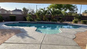 Una piscina con borde de baldosas, rodeada por un muro de ladrillo y varias plantas.