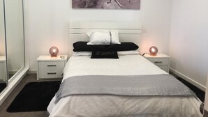 A bedroom with a white bed, black and white pillows, a silver throw, and a painting of horses on the wall. - Modern Cottage in peaceful setting, dog door to large fenced yard, farm walks.  (Mil-lel)
