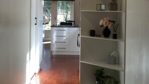 A hallway with wooden flooring, white walls, and a built-in shelving unit with decorative items. - Modern Cottage in peaceful setting, dog door to large fenced yard, farm walks.  (Mil-lel)