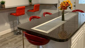 A kitchen with a granite countertop, red bar stools, a small island with a vase of flowers, and a white door. - Large Home Accommodates Up To 15 In Niagara USA (Niagara Falls)