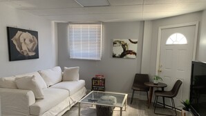 A living room with a white sofa, a glass coffee table, a TV, and a door with a window. - Large Home Accommodates Up To 15 In Niagara USA (Niagara Falls)