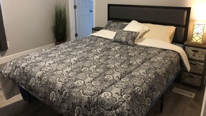 A bedroom with a patterned bedspread, a bedside table with a lamp, and a door leading to another room. - Large Home Accommodates Up To 15 In Niagara USA (Niagara Falls)
