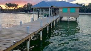 A wooden pier leading to a bungalow with a blue roof, surrounded by water and palm trees. - Live & Sleep over the Sea!! ** Glamping in Paradise** (San Pedro)