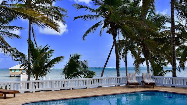 A pool area with a view of the ocean, surrounded by palm trees and a white fence. - Live & Sleep over the Sea!! ** Glamping in Paradise** (San Pedro)