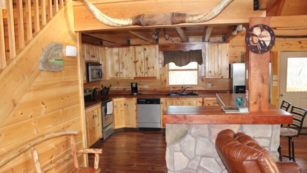 A wooden cabin interior with a kitchen, dining area, and a stone accent wall.