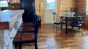 A wooden interior with a stone counter, a black refrigerator, a dining table with metal chairs, and a door with a window.