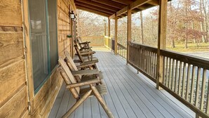 A wooden deck with a railing, a door, and a row of wooden chairs.