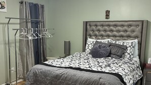Un dormitorio con cama, ventilador de techo, mesita de noche y estante en la pared.