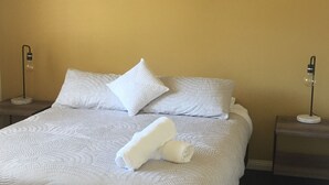 Ein ordentlich bezogenes Bett mit weißer Bettwäsche und Kissen, zwei Nachttischlampen und ein aufgerolltes Handtuch auf dem Bett.