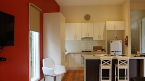 Une cuisine compacte avec des meubles blancs, une cuisinière encastrée, un réfrigérateur et un petit coin repas équipé de tabourets.
