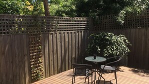 Eine Holzterrasse mit Tisch und Stühlen, umgeben von einem Holzzaun und Grünpflanzen.