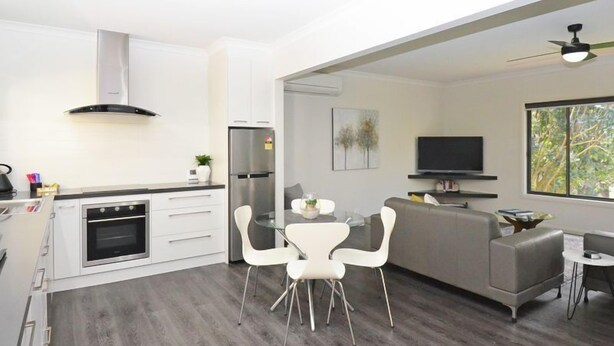 Una cucina moderna con forno a incasso, frigorifero e zona pranzo con tavolo in vetro e sedie bianche.