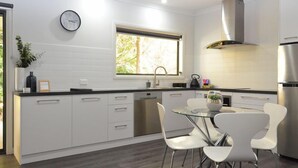 Una cucina moderna con mobili bianchi, un frigorifero in acciaio inossidabile, un tavolo da pranzo in vetro con sedie bianche e una finestra con vista sul verde.