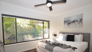 Una camera da letto con un'ampia finestra, una ventola a soffitto, un letto con molti cuscini e un quadro appeso alla parete.
