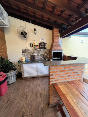 Un espace patio comprenant un four en briques, un ventilateur, un pare-feu en carreaux et un banc en bois.
