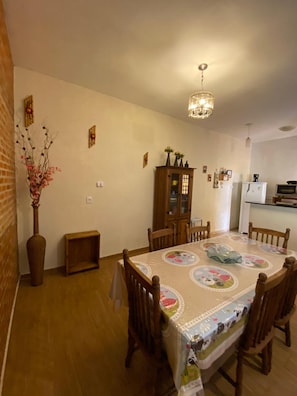 Un coin repas avec une table recouverte d’une nappe à motifs floraux, des chaises en bois, un buffet et un luminaire suspendu.