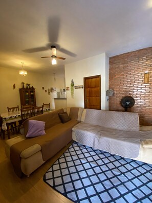 A living room with a sofa, a dining table with chairs, a ceiling fan, and a brick wall. - Rustic retreat in Brotas, SP + Private Pool + Air Conditioning (Brotas)