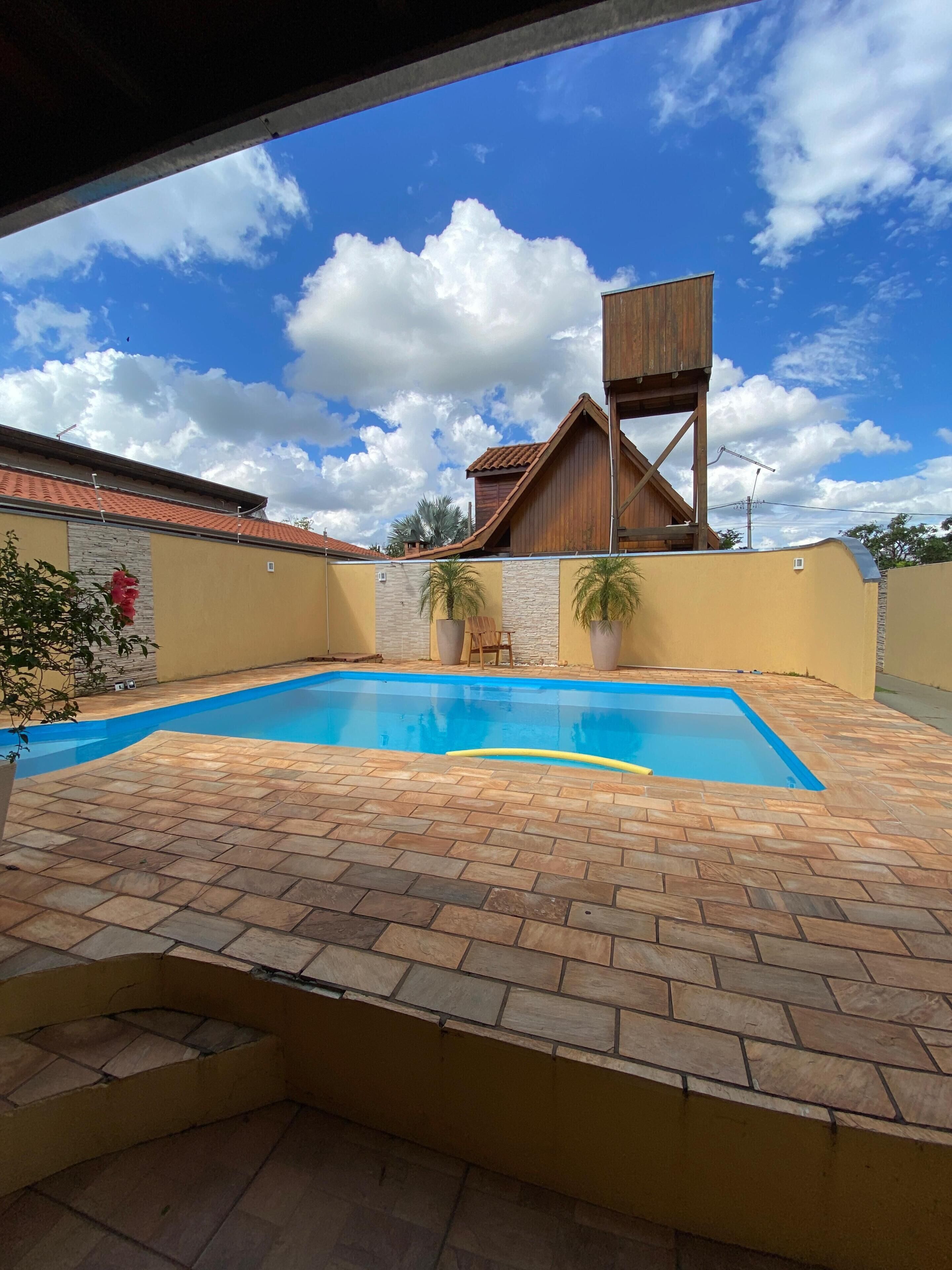 A swimming pool with a tiled deck, a wooden structure, and a clear sky.
