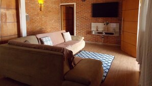 Een woonkamer met een bakstenen muur, een bank, een aan de muur bevestigde televisie en een houten deur.