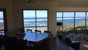 A dining area with a large table and chairs, overlooking a beach with waves. - Bluestone Bay - Port Fairy (Port Fairy)