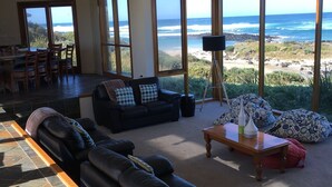 A spacious living area with a view of the ocean, a sofa, a coffee table, and a dining area with chairs. - Bluestone Bay - Port Fairy (Port Fairy)