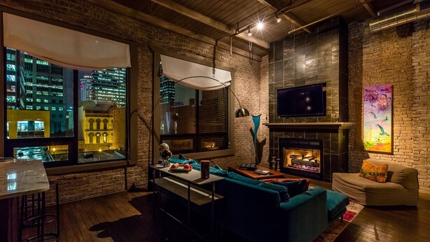 A modern living room with a fireplace, a large window overlooking a cityscape, and a cozy seating area. - City Loft PH*Walk to Broadway*Printers Alley Lofts (Nashville)