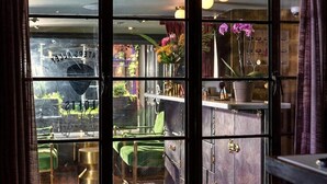 A room with a large window, a green chair, a cabinet with brass handles, and a vase with flowers. - City Loft PH*Walk to Broadway*Printers Alley Lofts (Nashville)
