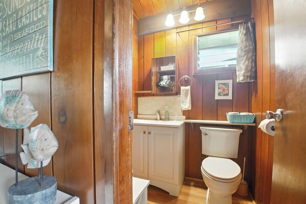 Een houten badkamer in een vakantiehuisje, met toilet, wastafel en een klein plankje met toiletartikelen.