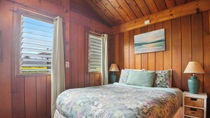 Ein Schlafzimmer einer Holzhütte mit einem Bett, zwei Nachttischen, einem Bild und einem Fenster mit Jalousien.