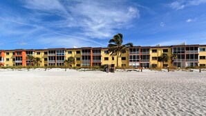 Un hotel frente a la playa con edificios de varios pisos, balcones y palmeras.
