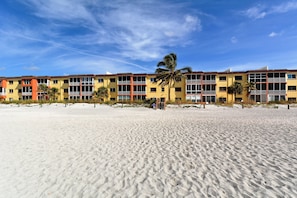 A beachfront hotel with multiple-story buildings, balconies, and palm trees.