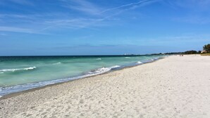 Una extensa playa de arena con olas suaves y un cielo azul despejado.