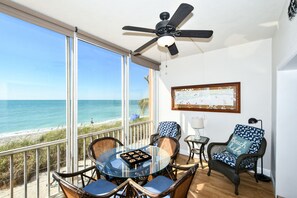A balcony with a glass table, wicker chairs, and a ceiling fan.