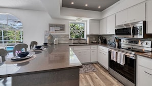 A modern kitchen with white cabinets, a large island, stainless steel appliances, and a view of a pool. - Relax in our PRIVATE Pool at Water View Villa (Venice)