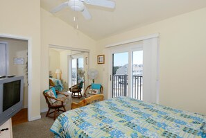 Una camera da letto con un letto, due sedie, una televisione, una ventola a soffitto e un balcone con vista.