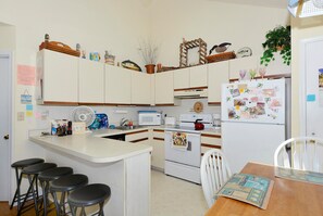 Cocina compacta con una isla central, microondas, estufa y refrigerador. Hay taburetes de bar y una mesa de comedor con sillas.
